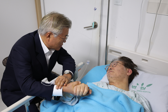 Former President Moon Jae-in, left, holds hands with Democratic Party leader Lee Jae-myung, right, at the Wonjin Green Hospital in Myeonmok-dong, Seoul, on Tuesday.[YONHAP]  
