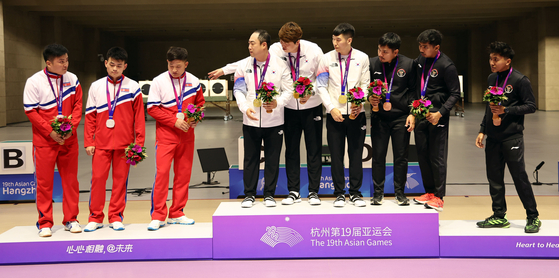 The South Korean men’s team that won the gold medal in the 10-meter target range running event, center, urges the North Korean team that won the silver medal, left, to join a group photo during the medal ceremony at Fuyang Yinhu Sports Center in Hangzhou, China, on Monday. The North Koreans refused the gesture. A similar situation happened in judo the same day when the North Korean judoka Kim Chol-gwang refused to shake the hand of his South Korean opponent, Kang Heon-cheol, in a round of 16 match in the men’s 76-kilogram division. The Asian Games in Hangzhou is the first international multi-sport event that the North Koreans have attended in five years since the Jakarta Palembang 2018 Asian Games [YONHAP] 