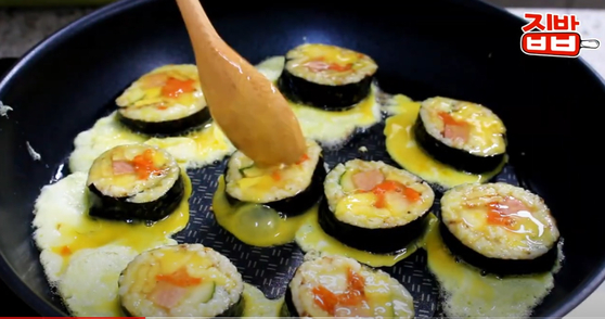 유튜브 영상에는 냉동 김밥이 한국에서 일반적으로 어떻게 먹는지 보여주며, 스크램블 에그에 담근 후 프라이팬에 던집니다. [SCREEN CAPTURE]
