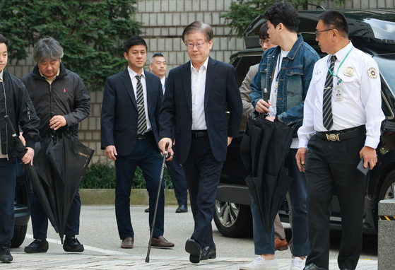 Democratic Party leader Lee Jae-myung, walking with a cane, enters the Seoul Central District Court in Seocho District in southern Seoul on Friday. [YONHAP]
