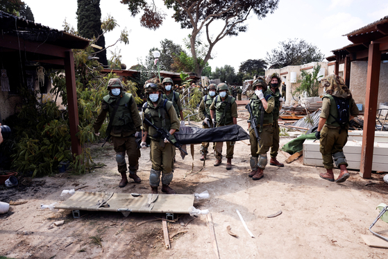 Israeli soldiers carry the body of a victim of an attack by Hamas militants at Kibbutz Kfar Aza, in southern Israel, on Tuesday. [REUTERS/YONHAP]