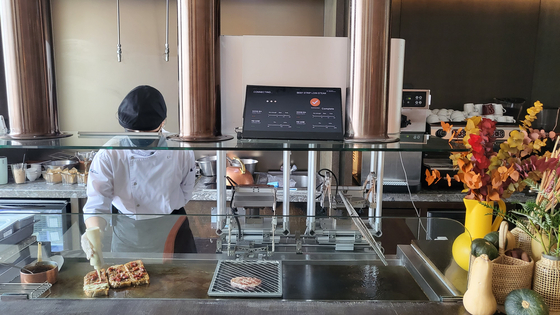 AI Chef Grill Robot, or ANDI, on the right, at Andaz Seoul Gangnam's dining venue Bites and Wine, cooks steaks to help the restaurant's human chef make its signature dish Andaz stAIk sandwich on Friday. [YIM SEUNG-HYE]