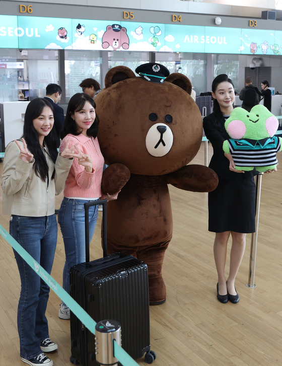 Air Seoul employees pose for a photo with Brown and lenini, characters from IPX, formerly known as Line Friends, next to the Air Seoul check-in counter at Incheon International Terminal on Monday. Air Seoul and IPX are joining forces for a co-marketing strategy, according to Air Seoul. [YONHAP]