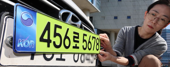 A sample of a light green license plate, which will be affixed to company-owned cars worth more than 80 million won ($59,799), is held up by a Ministry of Land, Infrastructure and Transport (MOLIT) official. MOLIT said it will pre-announce the amendment on Oct. 23, and implement it starting Jan. 1, 2024. The revision is intended to prevent business owners from evading taxes by purchasing luxury supercars as fleet vehicles and using them for personal use. A fleet vehicle is a type of car that is owned or leased by a business. [YONHAP]