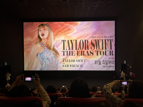 Taylor Swift fans take photos in front of the poster screening prior to the premiere of ″Taylor Swift: The Eras Tour″ at CGV Yongsan on Friday. [SHIN MIN-HEE]