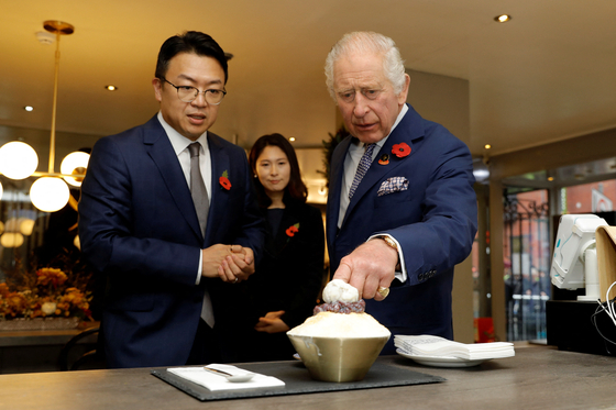King Charles speaks with the owners of a Korean dessert shop in New Malden, England, and points at bingsoo, or Korean shaved ice, on Wednesday during his visit to the Korean community there. [REUTERS]