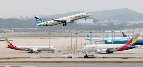 An Air Busan aircraft flies over planes from Korean Air and Asiana Airlines at Incheon International Airport on April 24. [YONHAP]