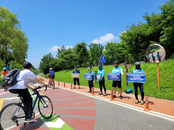 Volunteer bicycle patrol members hold signs urging cyclists to keep their speeds down.[SEOUL METROPOLITAN GOVERNMENT]