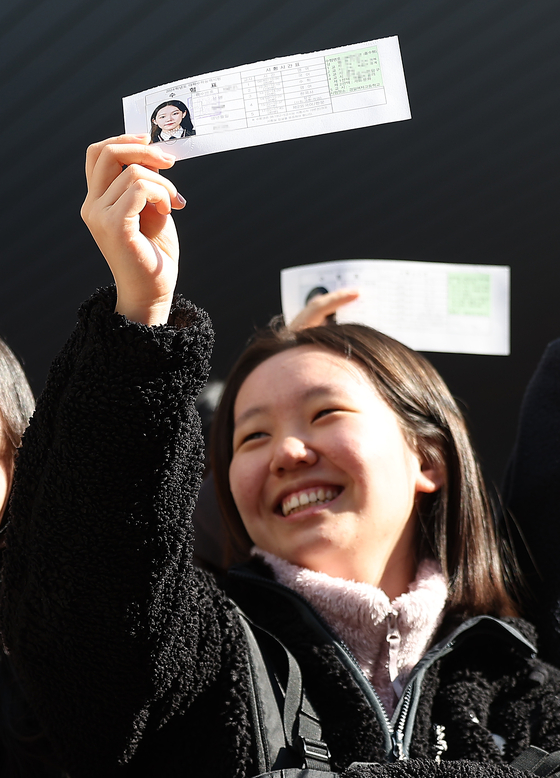 A test-taker smiles as she holds up a test slip verifying her identity at Kyungpook National University High School in Daegu on Wednesday, a day before the College Scholastic Ability Test (CSAT). The test-takers had an orientation to check their testing environment, including assigned seats. [YONHAP]