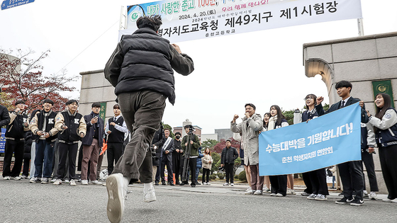 A taker of the college entrance exam runs to a test venue in Chuncheon, Gangwon, on Thursday morning as other sophomores and juniors wish him good luck. [YONHAP]