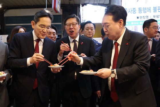 President Yoon Suk Yeol, right, shares bindaetteok, or mungbean pancakes, with Samsung Electronics Executive Chairman Lee Jae-yong, left, during a visit with business executives and Busan Mayor Park Heong-joon to Bupyeong Kkangtong Market in Busan Wednesday. [JOINT PRESS CORPS]