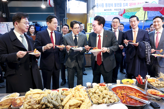 President Yoon Suk Yeol, fourth from right, and business leaders of major conglomerates eat tteokbokki, or spicy rice cakes, during a visit to Bupyeong Kkangtong Market in Busan on Wednesday. From left, SK Group Executive Vice Chairman Chey Jae-won, Samsung Electronics Executive Chairman Lee Jae-yong, Hyosung CEO and Chairman Cho Hyun-joon, Yoon, LG Chairman Koo Kwang-mo, Hanwha Group Vice Chairman Kim Dong-kwan and HD Hyundai Vice Chairman Chung Ki-sun. [JOINT PRESS CORPS]