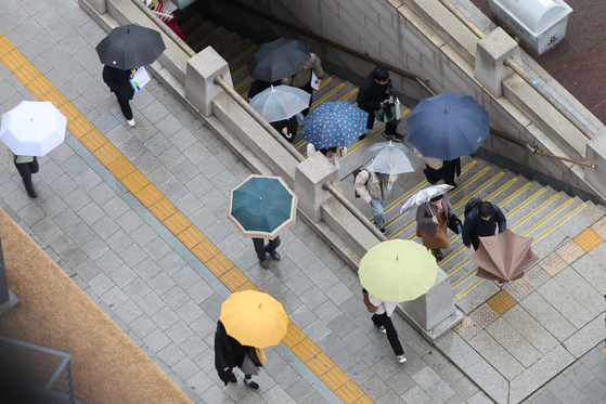 People use umbrellas as rain falls Monday morning at Seoul City Hall Station in Jung District, central Seoul. [YONHAP]