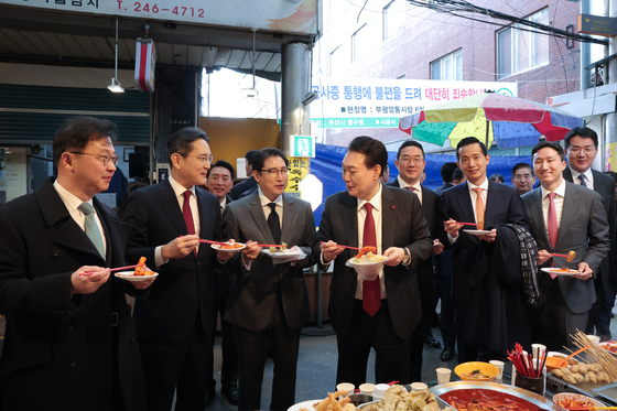 President Yoon Suk Yeol, fourth from left, and business leaders of major conglomerates eat tteokbokki, or spicy rice cakes, during a visit to Bupyeong Kkangtong Market in Busan on Wednesday. From left, SK Group Executive Vice Chairman Chey Jae-won, Samsung Electronics Executive Chairman Lee Jae-yong, Hyosung CEO and Chairman Cho Hyun-joon, Yoon, LG Chairman Koo Kwang-mo, Hanwha Group Vice Chairman Kim Dong-kwan, HD Hyundai Vice Chairman Chung Ki-sun and Hanjin Group Chairman Cho Won-tae. [JOINT PRESS CORPS]