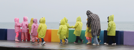 With winter rain pouring across the country, children in their pink and yellow raincoats watch the sea on the Dodu-dong Rainbow Coastal Road in Jeju Island on Thursday. The rain will continue until Friday nationwide. [NEWS1]