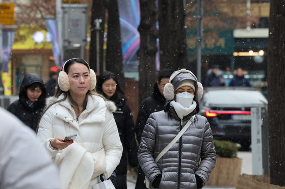 People walk in Myeong-dong, central Seoul, as snowflakes fall on Tuesday. [NEWS1]