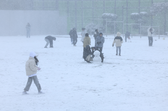 Students play in a snowy field at Halla Elementary School in Nohyeon-dong, Jeju, on Thursday. Flights at Jeju International Airport were delayed and canceled as the area saw heavy snow and wind shear the same day. [YONHAP] 