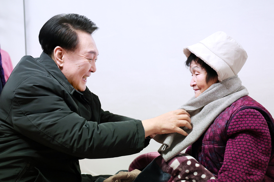 President Yoon Suk Yeol, left, helps a senior citizen wear a scarf at her home in Jungnang District, eastern Seoul, on Thursday. Yoon visited the woman to encourage her and provide winter supplies amid freezing temperatures this week. [PRESIDENTIAL OFFICE]