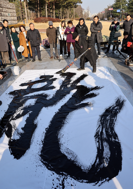 Lee Moo-ho, a calligraphist, wields a brush to celebrate the upcoming Year of the Dragon in front of the National Assembly in western Seoul on Tuesday. Lee is an instructor for the parliamentary calligraphy club. [YONHAP]