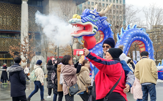 People snap a photo in front of the blue dragon display in Gwangwhamun in central Seoul on Sunday. The display celebrates the Year of the Dragon in 2024. [YONHAP]