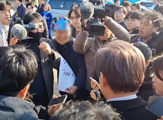 A man in blue paper crown approaches Democratic Party leader Lee Jae-myung at Gadeok Island in Busan on Tuesday. [YOUTUBE CAPTURE]