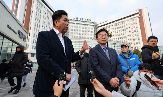 Democratic Party spokesman Kwon Chil-seung, left, speaks at a press briefing regarding party leader Lee Jae-myung's condition in front of Seoul National University Hospital in Jongno District, central Seoul, on Wednesday afternoon. [JOINT PRESS CORPS]