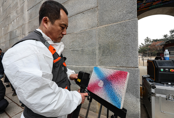 Lee Tae-jong, a researcher at the National Research Institute of Cultural Heritage, demonstrates how to remove spray paint from a stone slab by using a laser tool, in front of Yeongchu Gate at Gyeongbok Palace in Jung District, central Seoul, on Thursday. [NEWS1]