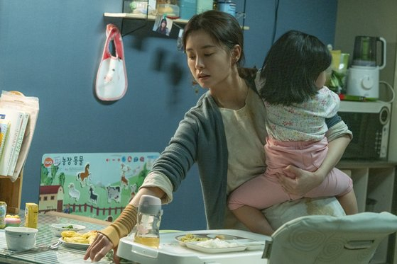 A scene in the movie "Kim Ji-young: Born 1982" featuring a mother working while taking care of her child. [TVING]