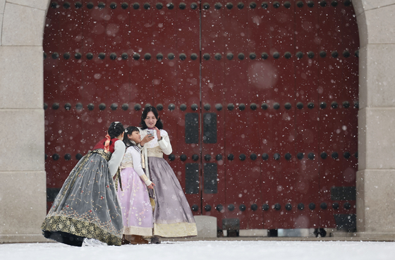 Tourists in hanbok, or Korean traditional dress, take photos near Gwanghwamun in Jongno District, central Seoul, as snow falls in the area on Tuesday. [YONHAP] 