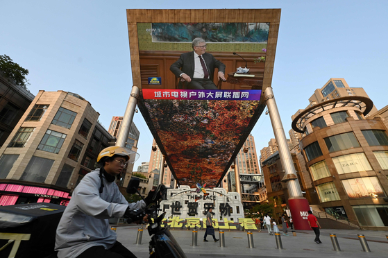 A China Central Television news broadcast shows footage of Microsoft co-founder Bill Gates during his meeting with Chinese President Xi Jinping (not seen), on a giant screen outside a shopping mall in Beijing on June 16, 2023. [Photo by GREG BAKER / AFP]
