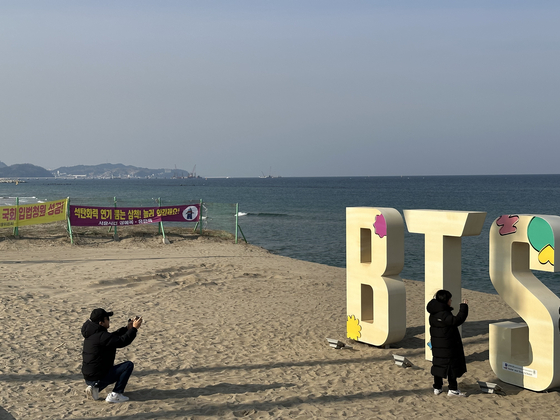 Tourists take photos near the BTS structure installed at Maengbang Beach in Samcheok, Gangwon, popular for being featured in boy band BTS's album ″Butter″ (2021). [JOONGANG PHOTO]