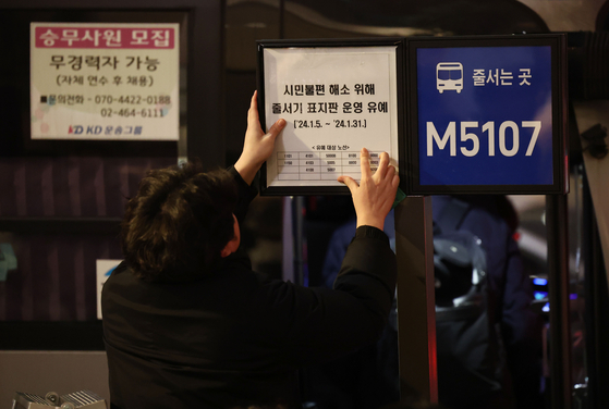 An employee at the Seoul Metropolitan Government posts a notice that the intercity bus signs will not be used through this month at the busy Myeong-dong bus stop in central Seoul on Jan. 5. [YONHAP] 