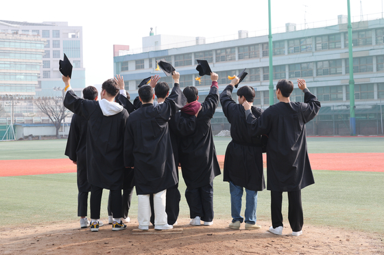 Graduates of Duksoo High School in Seongdong District, eastern Seoul pose for a photo on a pitching mound on the school’s field on Jan. 5. The high school’s liberal arts division relocated to Wirye New Town in Songpa District, southern Seoul, in 2022 and its special division, formerly known as the commercial division, will be annexed to Gyeonggi Commercial High school this year. [YONHAP]