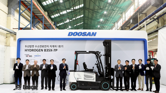 Doosan Bobcat Korea President Park Hyung-won, seventh from the left, takes a photo during a roll-out ceremony of Korea's first commercialized hydrogen fuel cell forklift, held at its production plant in Incheon on Monday, along with other attendees including Deputy Minister Lee Chang-heum of the Ministry of Environment, sixth from left. [DOOSAN BOBCAT]