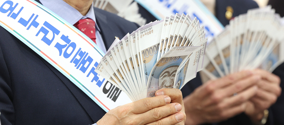 Attendees of an event to promote the use of Onnuri coupons, which are used to pay for goods at traditional markets and small shops at a discounted price, hold up the coupons at DGB Daegu Bank's Jung District Branch in Daegu on Wednesday, ahead of the Lunar New Year holiday. [YONHAP]