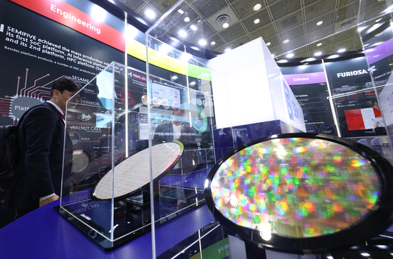 Visitors examine a semiconductor wafer at the Semiconductor Exhibition held at Coex, Gangnam, in October. [YONHAP]