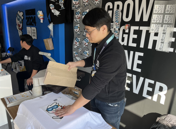 Lee Jin-sung, with production company Wongab Corporation, places a Moongcho sticker on a T-shirt for a customer at Gangneung Olympic Park in Gangneung, Gangwon on Wednesday. [MARY YANG]