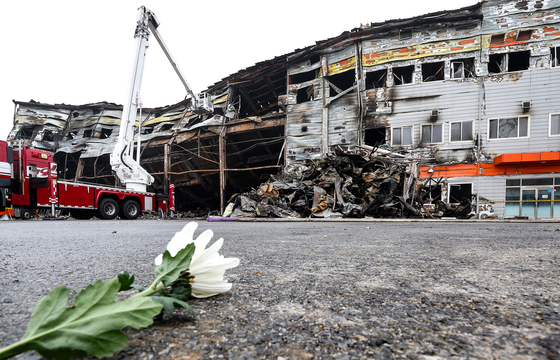 A chrysanthemum lies in front of the burnt-down four-story meat processing plant in Mungyeong, North Gyeongsang, on Thursday. Two firefighters lost their lives during the search for survivors. [YONHAP]