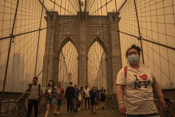 Pedestrians cross the Brooklyn Bridge as smoke from wildfires in Canada’s Quebec province blanketed New York on June 7, 2023. More than 125 million Americans will be exposed to unhealthy levels of air pollution by the middle of the century, largely because of increased smoke from wildfires, according to new estimates. [Dave Sanders/The New York Times]