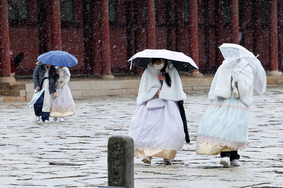Tourists wearing hanbok, or Korean traditional dress, walk in the snow as it falls at Gyeongbok Palace in Jongno District, central Seoul, on Wednesday. [NEWS1]