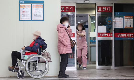 A patient in a wheelchair and a guardian wait in front of an emergency medical center in Seoul on Wednsday morning. Around 71 percent of interns and residents at 100 major hospitals nationwide submitted their resignation letters as of 10 p.m. Tuesday to protest the government's medical school enrollment quota hike. [YONHAP] 
