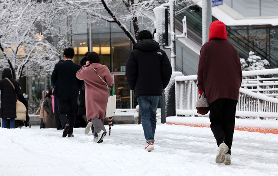 Pedestrians walk on a street covered in snow on Thursday morning in central Seoul. [NEWS1]