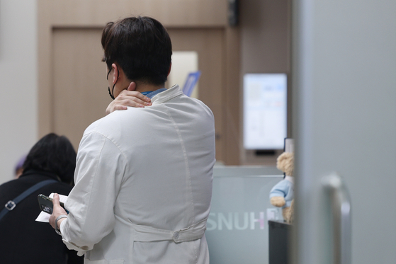 A doctor massages his shoulder as he stands at a university hospital in Seoul on Friday. The government on the same day raised its national health crisis warning to the highest ″serious″ level as mass resignations of trainee doctors continued. [YONHAP] 
