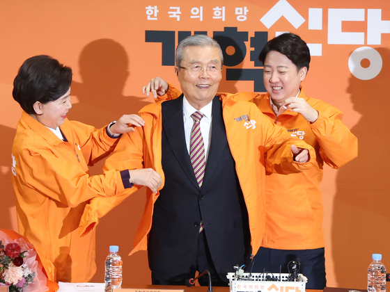 Veteran politician Kim Chong-in, center, dubbed “kingmaker” for his election engineering experience, receives an orange party jacket from leader Lee Jun-seok, right, during a supreme council meeting at the National Assembly in western Seoul on Monday. He was named as the party’s new nomination committee chief ahead of the April 10 general elections last Friday. [NEWS1]