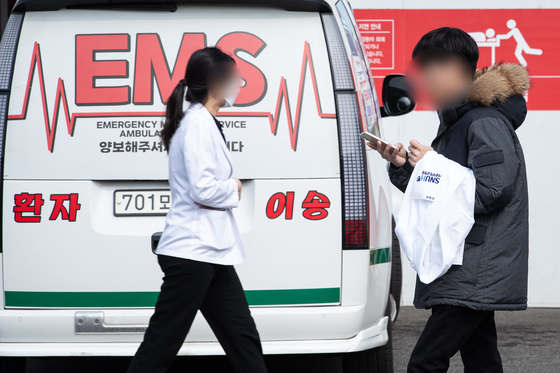 Medical professionals walk in front of a parked ambulance in a hospital in downtown Seoul on Sunday. [NEWS1] 