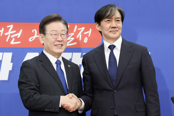 Democratic Party leader Lee Jae-myung, left, shakes hands with former Justice Minister Cho Kuk at the National Assembly in western Seoul on Tuesday. [JUN MIN-KYU]