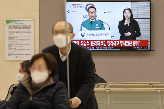 A patient and her guardian at a hospital in Seoul pass by a television screen broadcasting the government's press briefing on trainee doctors' strike on Tuesday. [NEWS1]