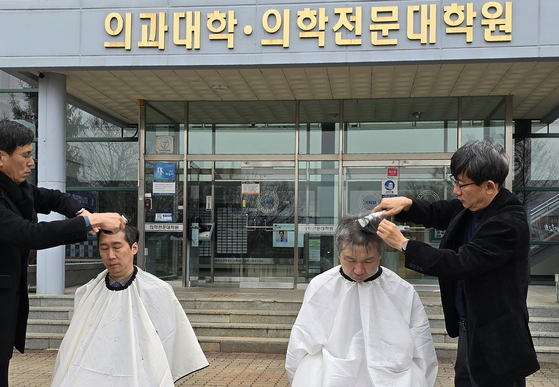 Medical professors at Kangwon National University shave their heads in front of the school on Tuesday to protest the university's request to increase its enrollment quota from 49 to 140. [KANGWON NATIONAL UNIVERSITY]