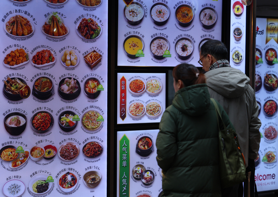 Tourists to Korea look at the menu outside a restaurant in Jung District, central Seoul, on Thursday. The price of dining out in Korea jumped by 3.8 percent in February compared to the year before, more than the 3.1 percent increase in inflation during the same period, according to Statistics Korea. [YONHAP]