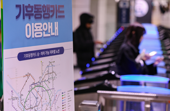 Commuters pass through subway turnstiles at the platform of City Hall Station in downtown Seoul, next to a banner guiding how to use the Climate Card on Monday. [NEWS1]